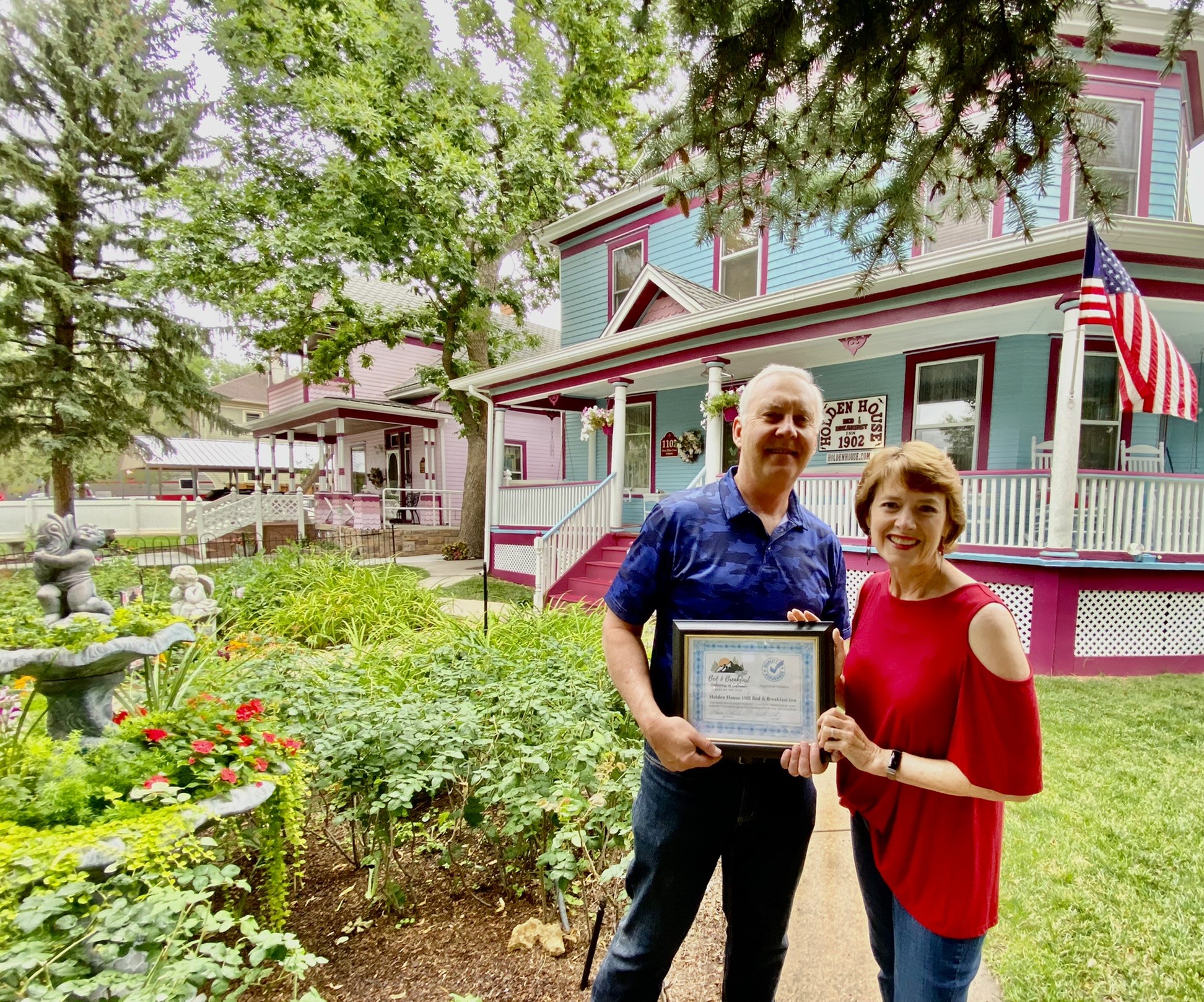 Holden House innkeepers Sallie and Welling Clark proudly display their membership certificate for guest service and quality assurance in the front garden at the inn.